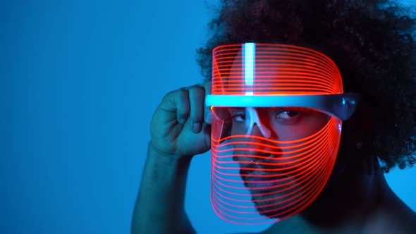 Man wearing light therapy mask against blue wall alt