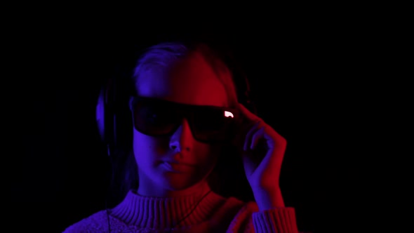 Happy Girl Listening Music in Headphones and Black Sunglasses in Dark Studio with Red and Blue alt
