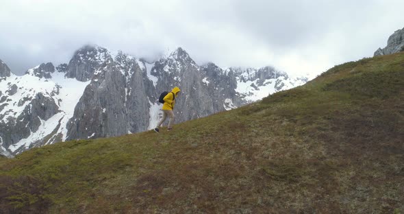 Hiker Goes on a Hill Against the Background of Snow-capped Mountains