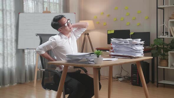 Asian Man Having Backache While Working Hard With Documents At The Office alt