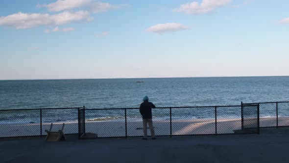 Man Overlooking Beach on Boardwalk With Fence Aerial 1