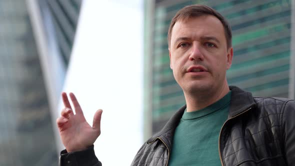 Businessman Standing Outdoors with Office Building in Background Looking at Camera and Talking alt