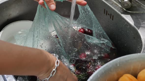 Female Hands Wash Cherries with Water Using a Plastic Bag and Drain the Water Into the Sink