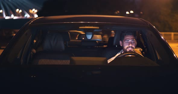 Man Using Mobile Phone Sitting in Car Outdoors at Night alt