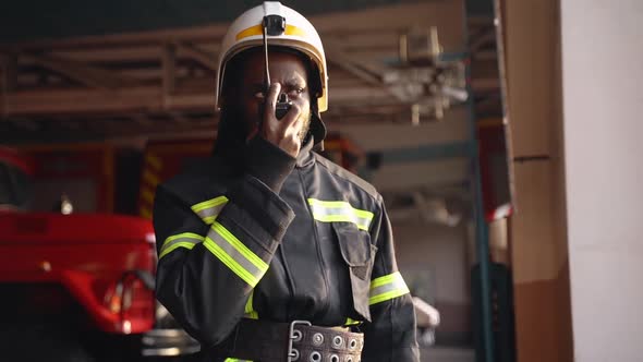 African American Fireman in Equipment with Helmet Use Walkie Talkie at the Station alt