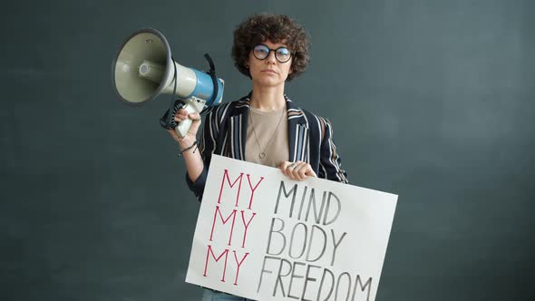 Portrait of Strong Woman Holding My Freedom Banner and Megaphone Standing on Black Background alt