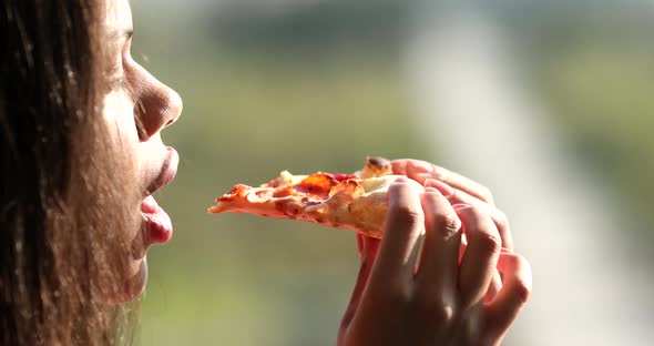 Close up portrait of young African woman eating slice of pizza at home.