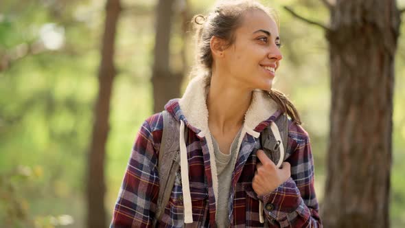 Motion Portrait Smiling Traveler Woman in Woods with Backpack, Hiking in Forest at Autumn. alt