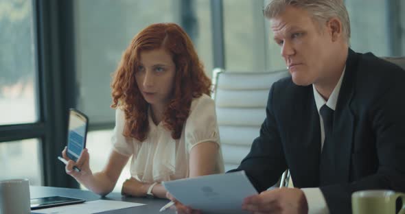 A businesswoman showing a new add on her phone to her business colleagues during a marketing meeting alt