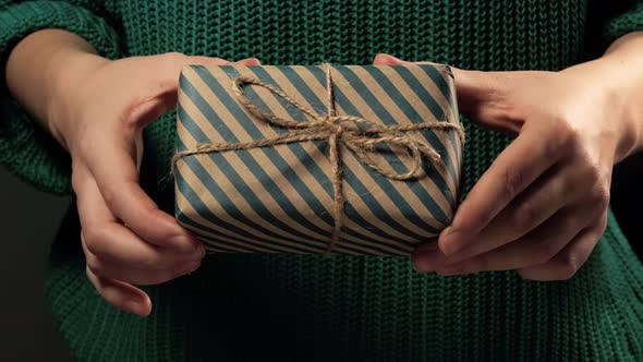 Girl  hand holding a gift wrapped in striped green-brown paper tied with a rope