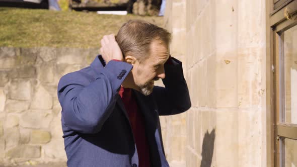 A Middleaged Caucasian Man Fixes His Hair and Jacket and Looks Into the Reflection in a Window