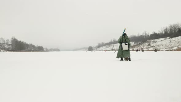 Fisherman with ice drill and fishing equipment is walking along frozen ice lake alt