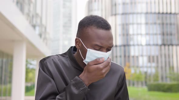 A Young Black Man in a Face Mask Is Sick, Coughs, Has a Headache and Sweats - Office Buildings alt