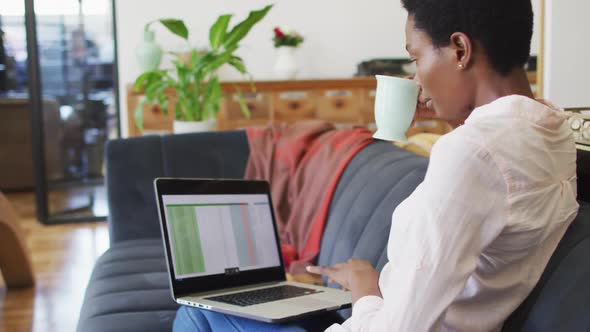Happy african american woman sitting on sofa in living room, using laptop alt