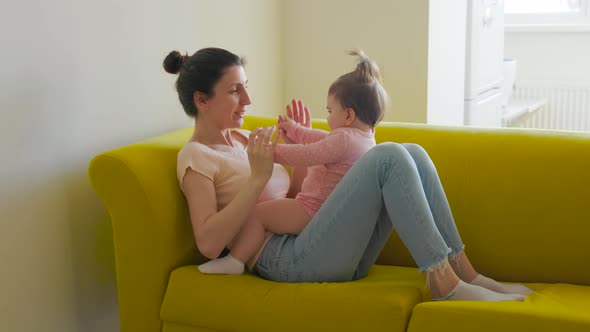 Authentic of Young Mother is Playing with Her Baby Siting on the Yellow Sofa in a Morning alt
