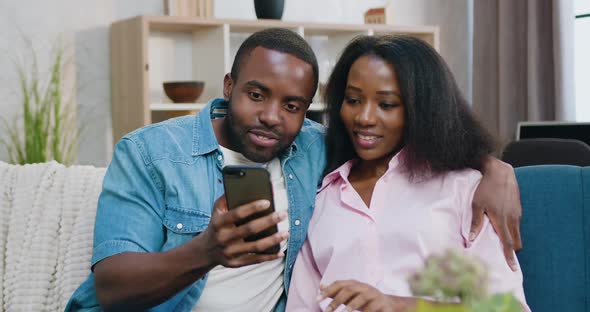 Couple Sitting Together on Comfortable Sofa at Home and Browsing Mobile Apps alt