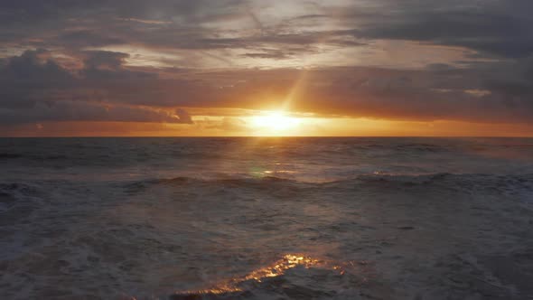 Small Sea Waves Crashing Ashore with Beautiful Golden Sunset in the Background alt