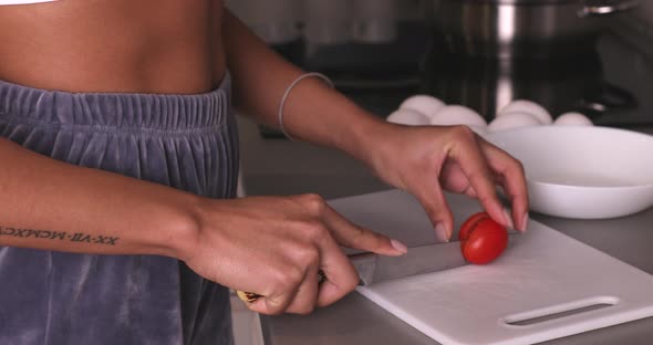 Black woman's hands using kitchen knife cutting fresh tomato.