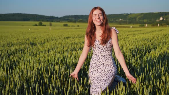 Ginger Woman Walking Through Wheat Field at Sunset Touching Green Ears of Wheat alt
