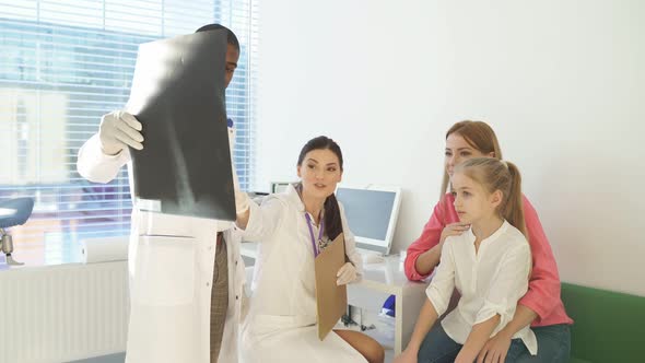Pediatrician Explaining and Showing Lung Xray for Sick Child and Mother in Hospital Office