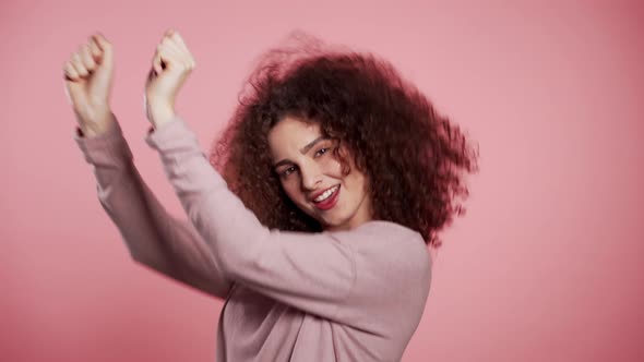 Beautiful Woman with Curly Hair Dancing with Head on Pink Studio Background. alt