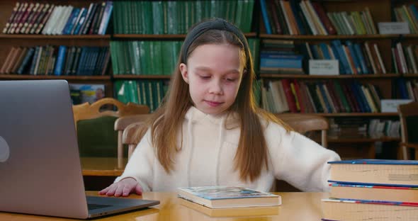 A Little Girl Is Coming To the Desk with the Book and Opens It. Reading Room in the Library.  alt