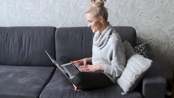 Cheerful Young Blond Woman Sitting on Couch in Living Room and Using Laptop alt