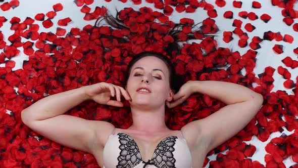 An attractive woman laying on the floor with red rose petals all around her
