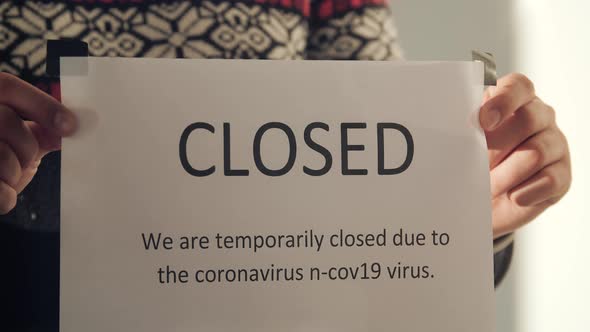 Close Up Business Owner Puts Closed Sign on Glass Door Due to Coronavirus alt