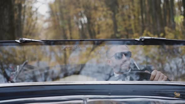 Portrait Through Windscreen of Rich Man in Sunglasses Sitting at Handlebar alt