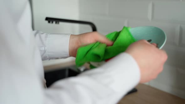 A man cleans a washed plate in a modern kitchen. You can see the towel, plate, hands and sink alt
