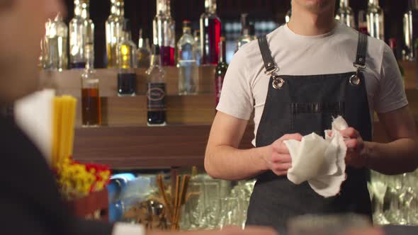 Pan Footage, Man Drinks Alcohol and Talks To Bartender Who Wipes a Glass