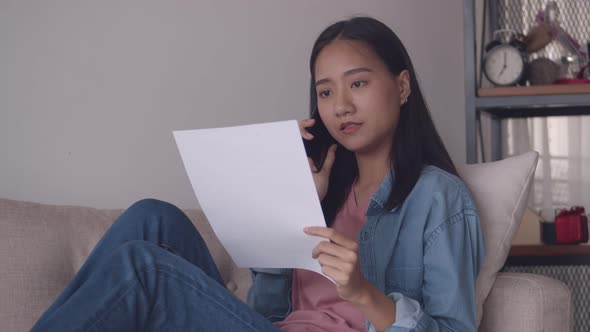 Young Asian woman talking on Phone and reading documents While sitting sofa.