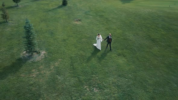 Husband and wife in love are walking hand in hand through a well-kept garden of trees and bushes