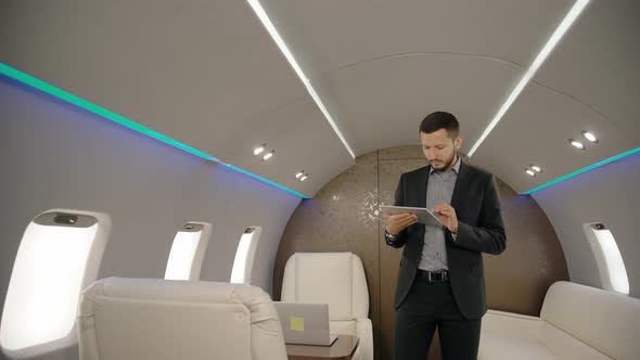 Young Confident Chief Banker Director Businessman Using Tablet, Walking Along Airplane Interior.