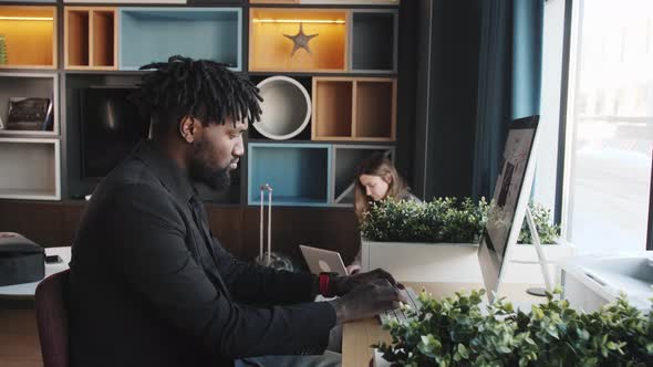 Darkskinned Business Man in a Dark Suit Works at a Computer in a Modern Office alt