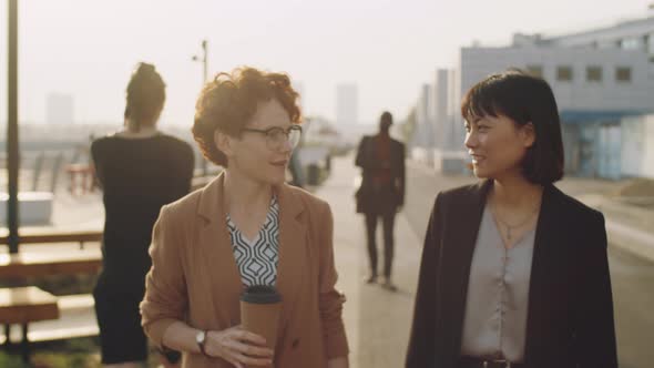 Multiethnic Female Colleagues Walking in City and Talking alt