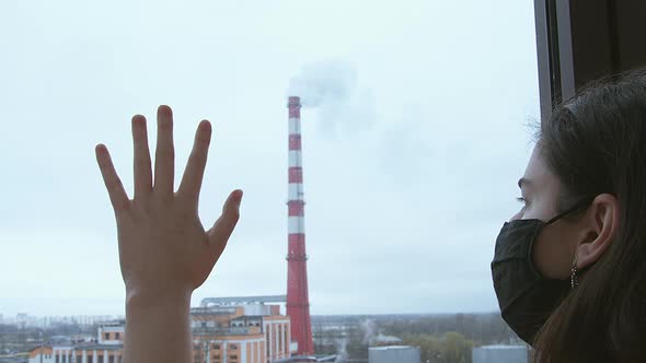 A Girl in a Black Mask Looks Out the Window Putting Her Hand on the Glass