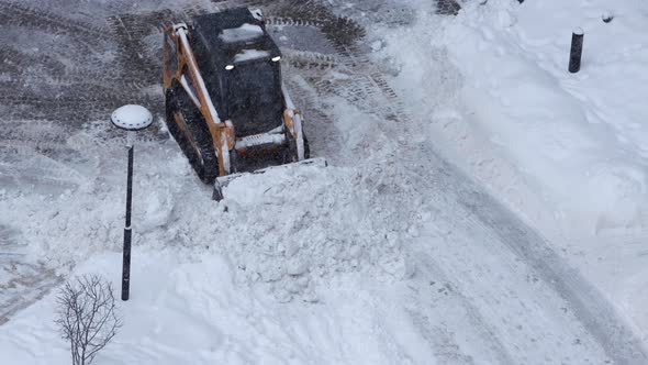 Crawler Yellow Black Excavator Removes Snow with a Snow Plow While Snowfall alt