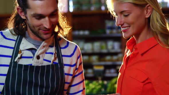 Male staff assisting woman in selecting fresh vegetables alt