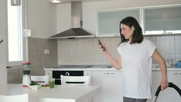 Young woman in white t-shirt in wireless headphones vacuuming home in the kitchen alt