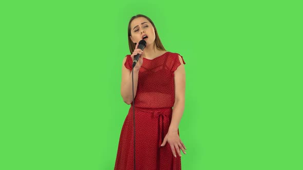 Tender Girl in Red Dress Is Singing Into a Microphone and Moving To the Beat of Music. Green Screen alt