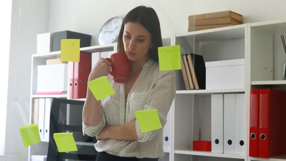 Businesswoman in White Blouse Considering Stickers on Glass in Office