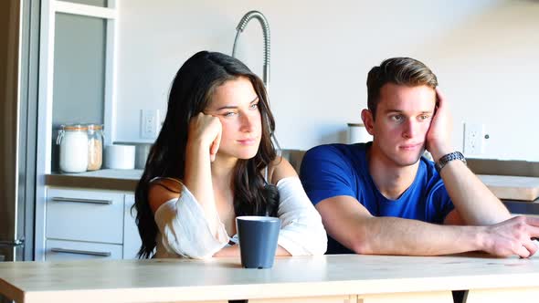 Thoughtful couple sitting in kitchen alt