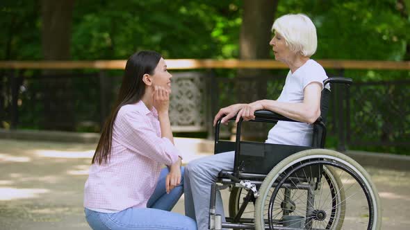 Smiling Volunteer Talking With Old Woman in Wheelchair, Disabled People Support alt