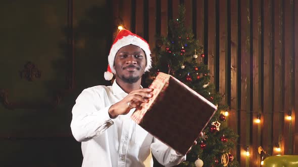 African Man with a Gift in Hands on Background of Christmas Tree.