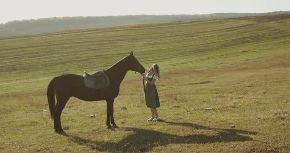 Happy Slavic Woman in Dress Caresses a Brown Horse Among the Wide Steppes alt