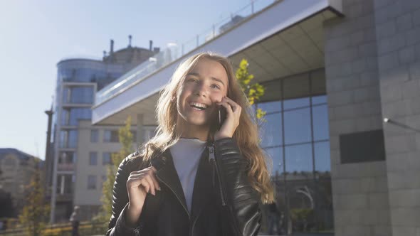 Beautiful Young Woman is Walking on the City Street While Talking with Her Friend on the Smartphone alt