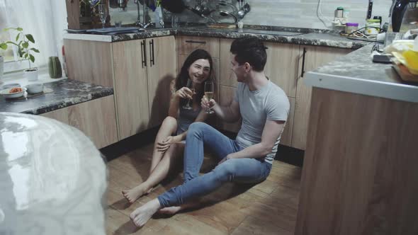 Affectionate Young Family Couple Sitting on the Floor of Cozy Kitchen and Celebrating Anniversary alt