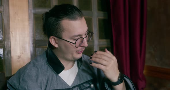 Young Guy with Fashionable Hairstyle and Glasses Blows on His Fingers Because He Has Covered Nails